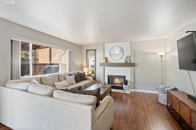 living room featuring dark wood-style floors, a large fireplace, and baseboards