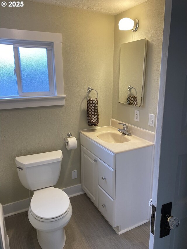 bathroom with vanity, toilet, wood finished floors, and baseboards