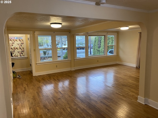 unfurnished room with baseboards, arched walkways, ornamental molding, dark wood-type flooring, and a textured ceiling