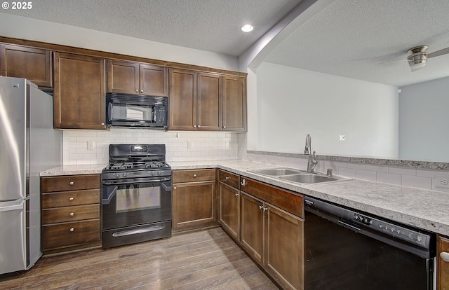 kitchen featuring dark wood-type flooring, light countertops, arched walkways, black appliances, and a sink