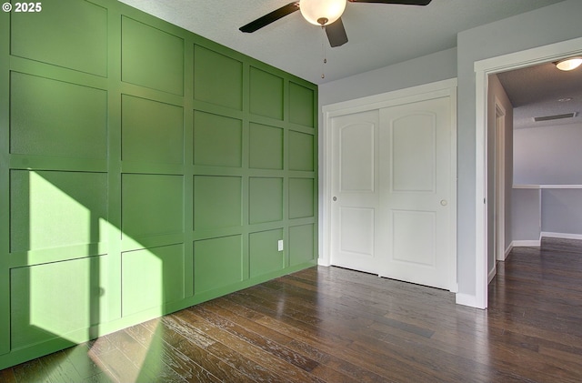 unfurnished bedroom with visible vents, ceiling fan, dark wood-type flooring, a closet, and a decorative wall