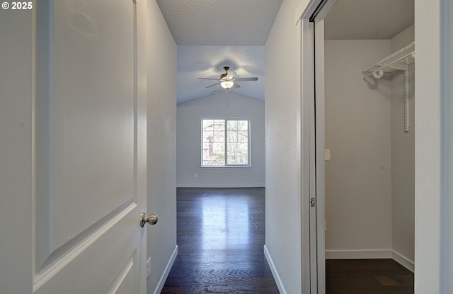 hallway featuring vaulted ceiling, a textured ceiling, baseboards, and dark wood-style flooring