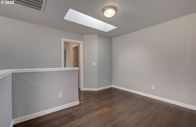 empty room featuring dark wood finished floors, visible vents, a skylight, and baseboards