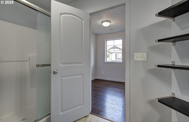 bathroom featuring an enclosed shower, baseboards, a textured ceiling, and wood finished floors