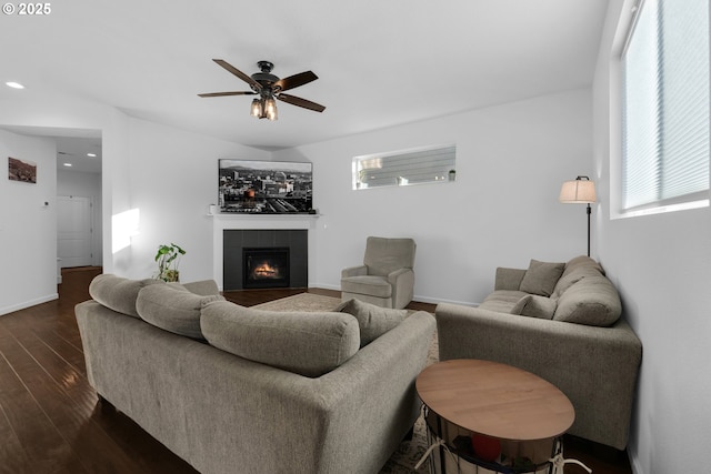 living room with a tiled fireplace, a healthy amount of sunlight, dark wood-type flooring, and ceiling fan