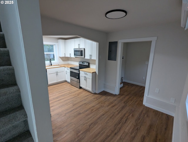 kitchen featuring white cabinetry, butcher block counters, appliances with stainless steel finishes, electric panel, and sink