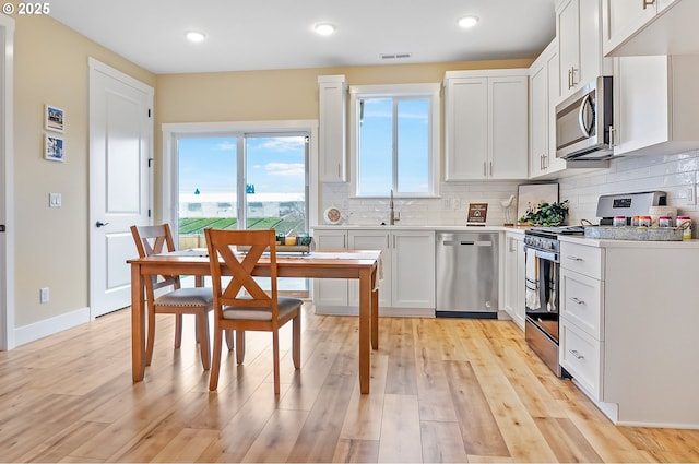 kitchen with white cabinetry, visible vents, appliances with stainless steel finishes, light wood-type flooring, and decorative backsplash