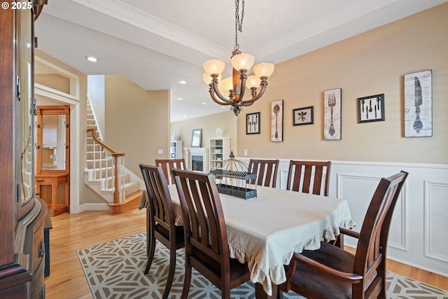 dining space with a chandelier, stairway, light wood finished floors, recessed lighting, and a wainscoted wall