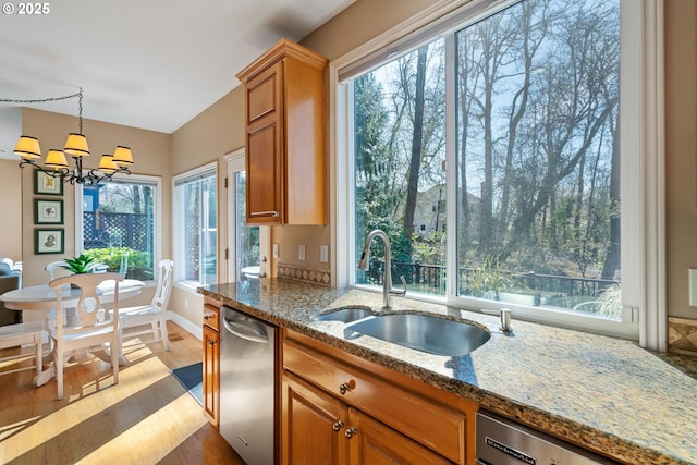 kitchen featuring an inviting chandelier, a sink, dishwashing machine, brown cabinets, and stainless steel dishwasher