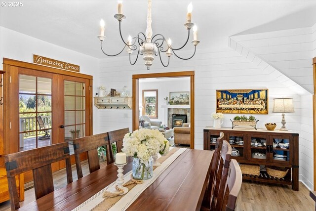 dining area with a chandelier, healthy amount of natural light, french doors, wood finished floors, and wooden walls
