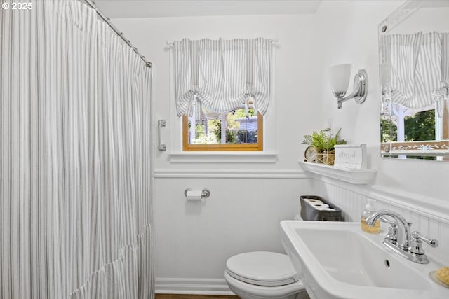 bathroom with a sink, toilet, wainscoting, and a shower with curtain