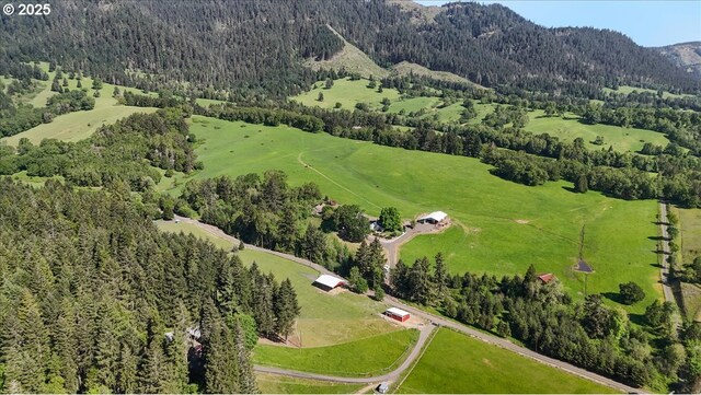 aerial view of property and surrounding area with a forest, a mountain backdrop, and rural landscape