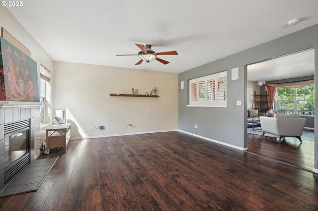 unfurnished living room with ceiling fan, a tiled fireplace, baseboards, and hardwood / wood-style flooring