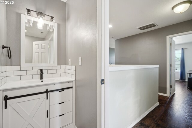 bathroom with vanity, baseboards, decorative backsplash, wood finished floors, and visible vents