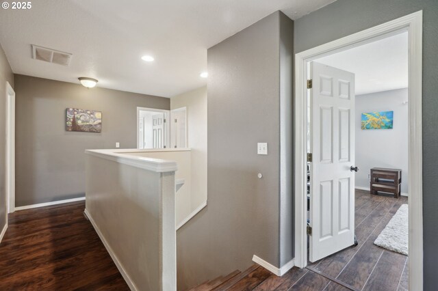 corridor featuring visible vents, dark wood finished floors, baseboards, an upstairs landing, and recessed lighting