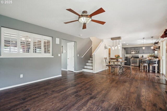 living room featuring baseboards, dark wood finished floors, ceiling fan, and stairs