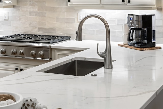 interior details with light stone counters, decorative backsplash, white cabinetry, and stainless steel gas stovetop