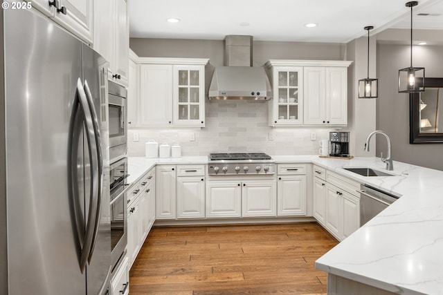 kitchen featuring appliances with stainless steel finishes, white cabinets, light wood-type flooring, a peninsula, and wall chimney exhaust hood