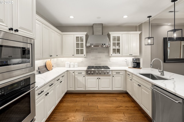 kitchen featuring appliances with stainless steel finishes, white cabinets, a sink, wood finished floors, and wall chimney exhaust hood