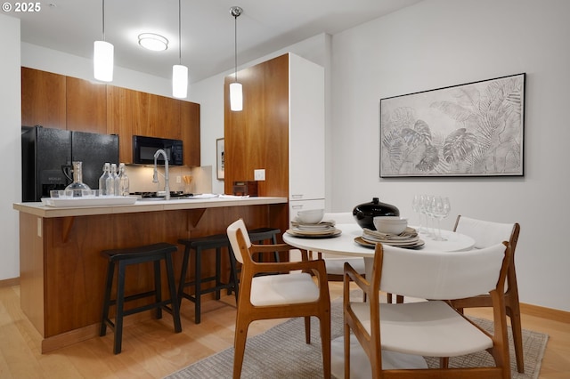 kitchen with hanging light fixtures, black appliances, kitchen peninsula, and light hardwood / wood-style flooring