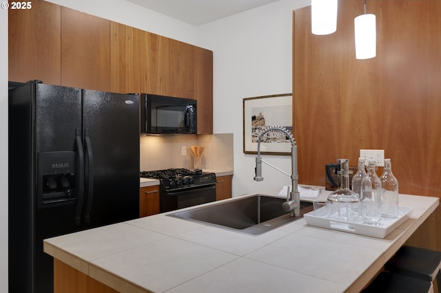 kitchen featuring sink, black appliances, pendant lighting, and tile counters