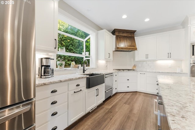 kitchen featuring appliances with stainless steel finishes, wood finished floors, a sink, white cabinets, and custom range hood