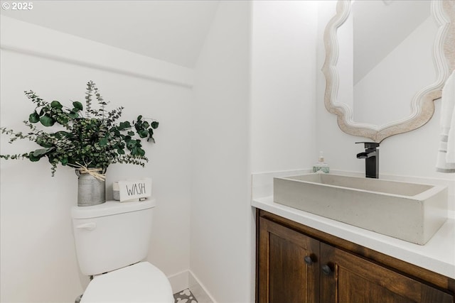 half bathroom featuring toilet, baseboards, and vanity