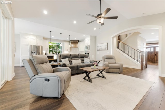 living area with wood finished floors, ceiling fan, stairway, recessed lighting, and arched walkways