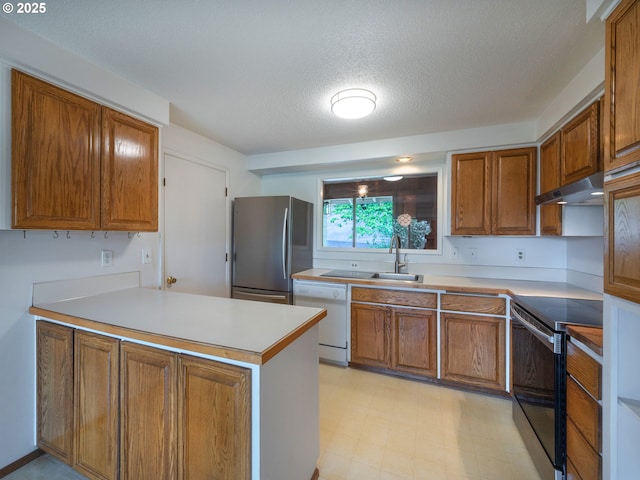 2830 Capital Dr, Eugene, OR 97403 - kitchen with stainless steel appliances, a peninsula, brown cabinetry, under cabinet range hood, and a textured ceiling