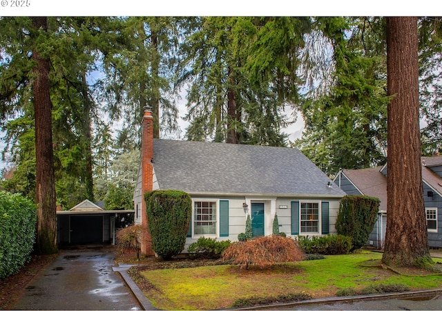 view of front of home with driveway, a chimney, an attached carport, roof with shingles, and a front yard