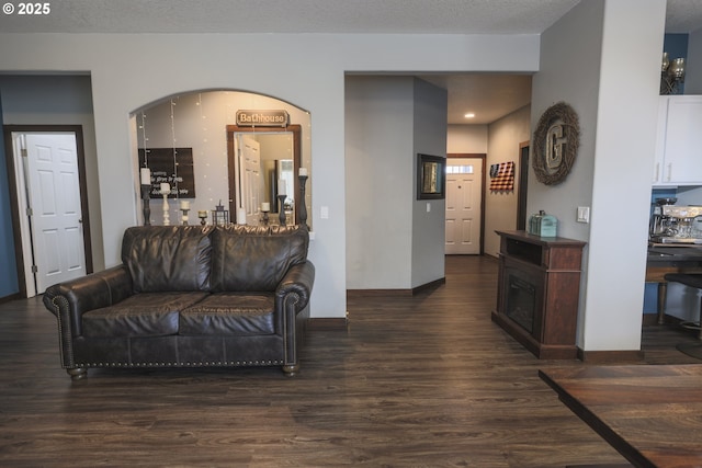 living area featuring arched walkways, a fireplace, a textured ceiling, wood finished floors, and baseboards