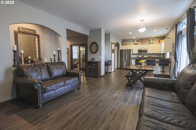 living room with dark wood-style floors, arched walkways, and a textured ceiling