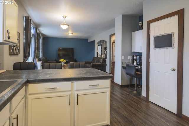 kitchen featuring tile countertops, open floor plan, dark wood-style flooring, a peninsula, and white cabinetry