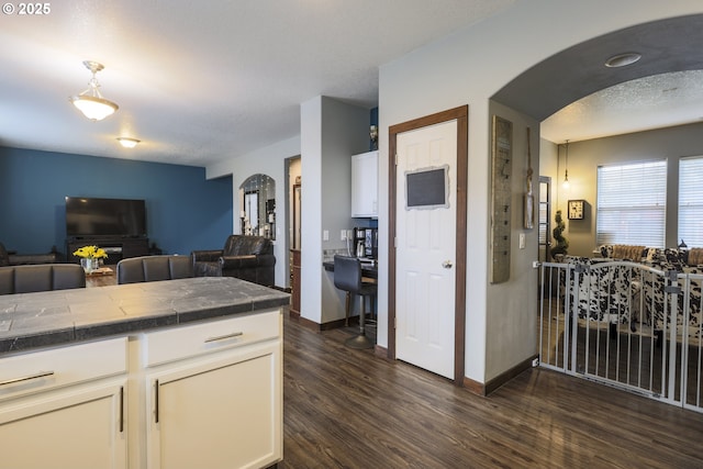 kitchen with white cabinetry, arched walkways, open floor plan, and dark wood-style flooring