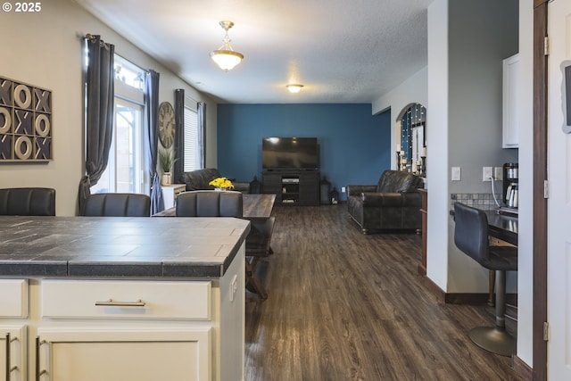 interior space with a textured ceiling, baseboards, open floor plan, white cabinets, and dark wood finished floors