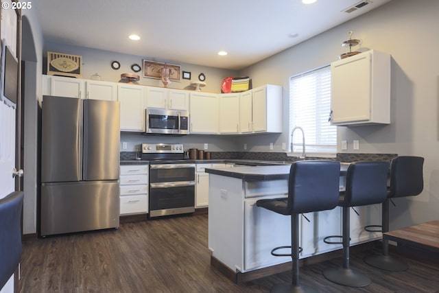 kitchen with a peninsula, appliances with stainless steel finishes, dark countertops, and visible vents