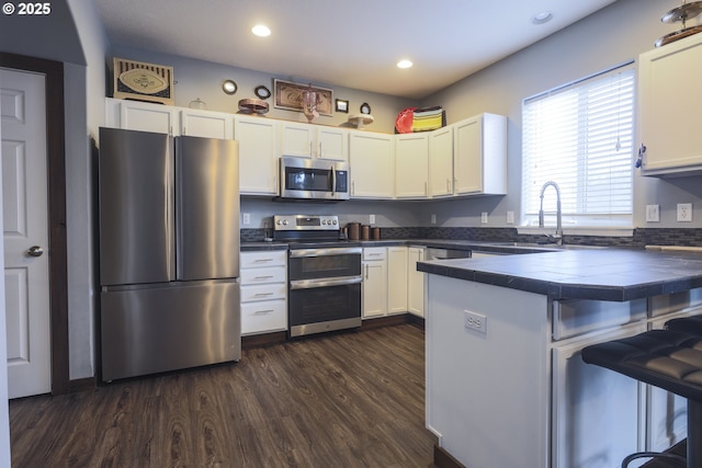 kitchen with white cabinets, a peninsula, stainless steel appliances, a kitchen bar, and a sink