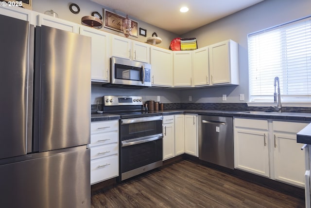 kitchen with appliances with stainless steel finishes, dark countertops, white cabinetry, and a sink