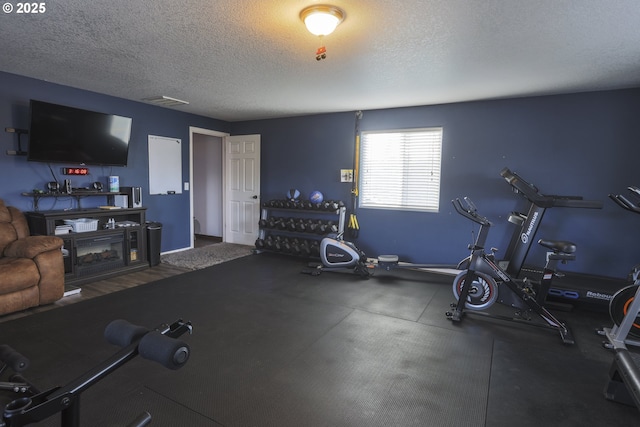 exercise room with a textured ceiling, a fireplace, and visible vents