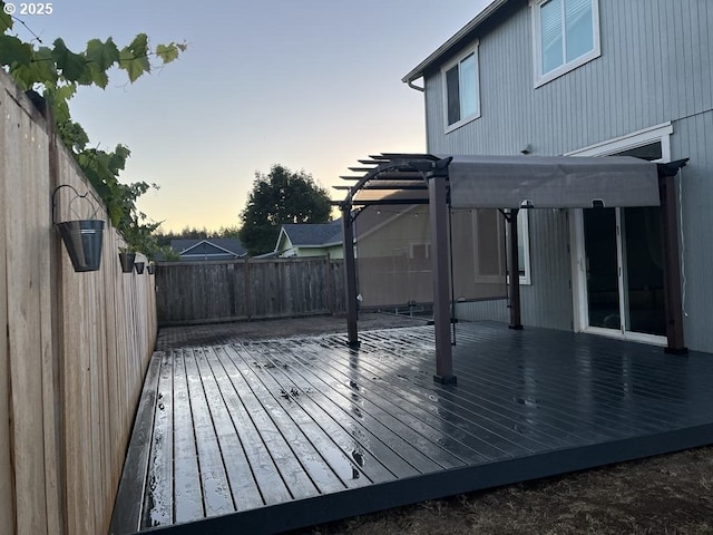 deck at dusk featuring a fenced backyard and a pergola