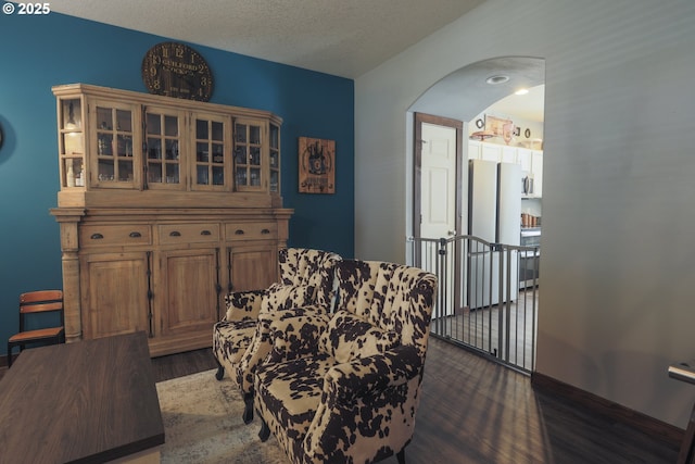 sitting room featuring arched walkways, dark wood-type flooring, and a textured ceiling