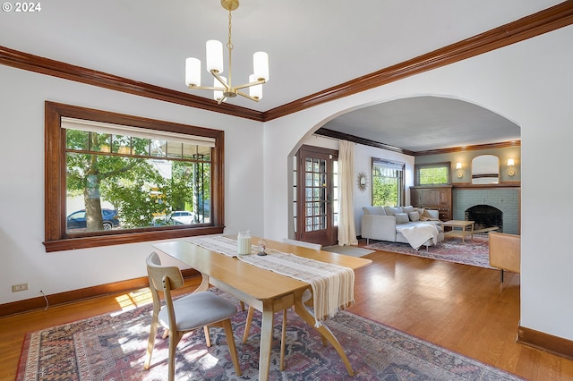 dining area with crown molding, arched walkways, an inviting chandelier, and wood finished floors