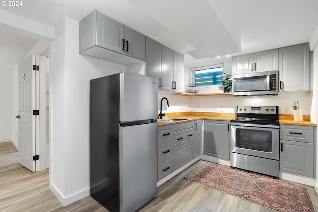 kitchen featuring stainless steel appliances, wood counters, light wood finished floors, a sink, and gray cabinetry