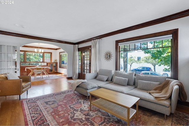 living room featuring an inviting chandelier, wood finished floors, ornamental molding, and arched walkways