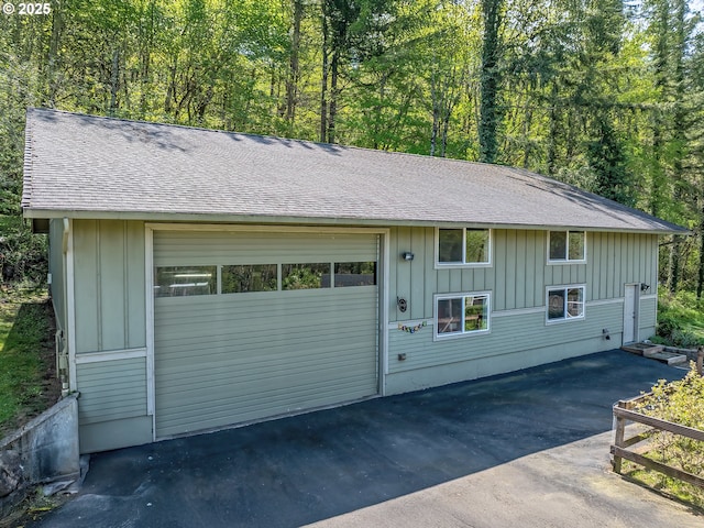 view of front of home featuring roof with shingles, a garage, board and batten siding, a view of trees, and driveway