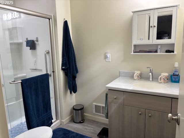 89384 Sutton Lake Rd, Florence, OR 97439 - full bathroom with vanity, a stall shower, baseboards, wood finished floors, and toilet