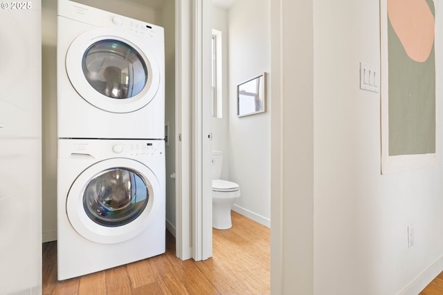 clothes washing area featuring baseboards, stacked washer / drying machine, wood finished floors, and laundry area