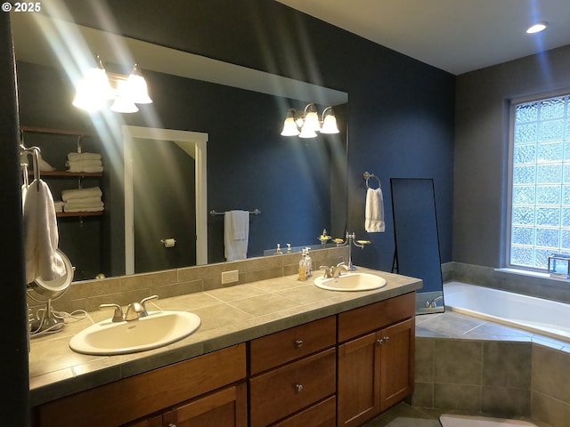 bathroom with vanity, a relaxing tiled tub, and an inviting chandelier