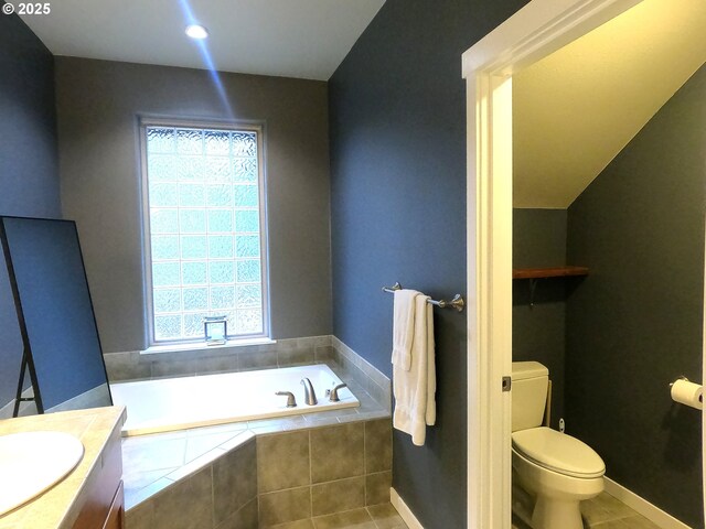 bathroom featuring tile patterned flooring, vanity, tiled bath, and toilet