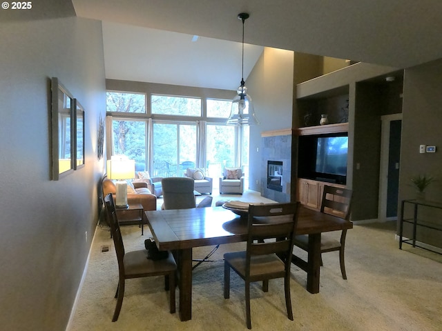 dining area featuring a tiled fireplace, a high ceiling, and light carpet